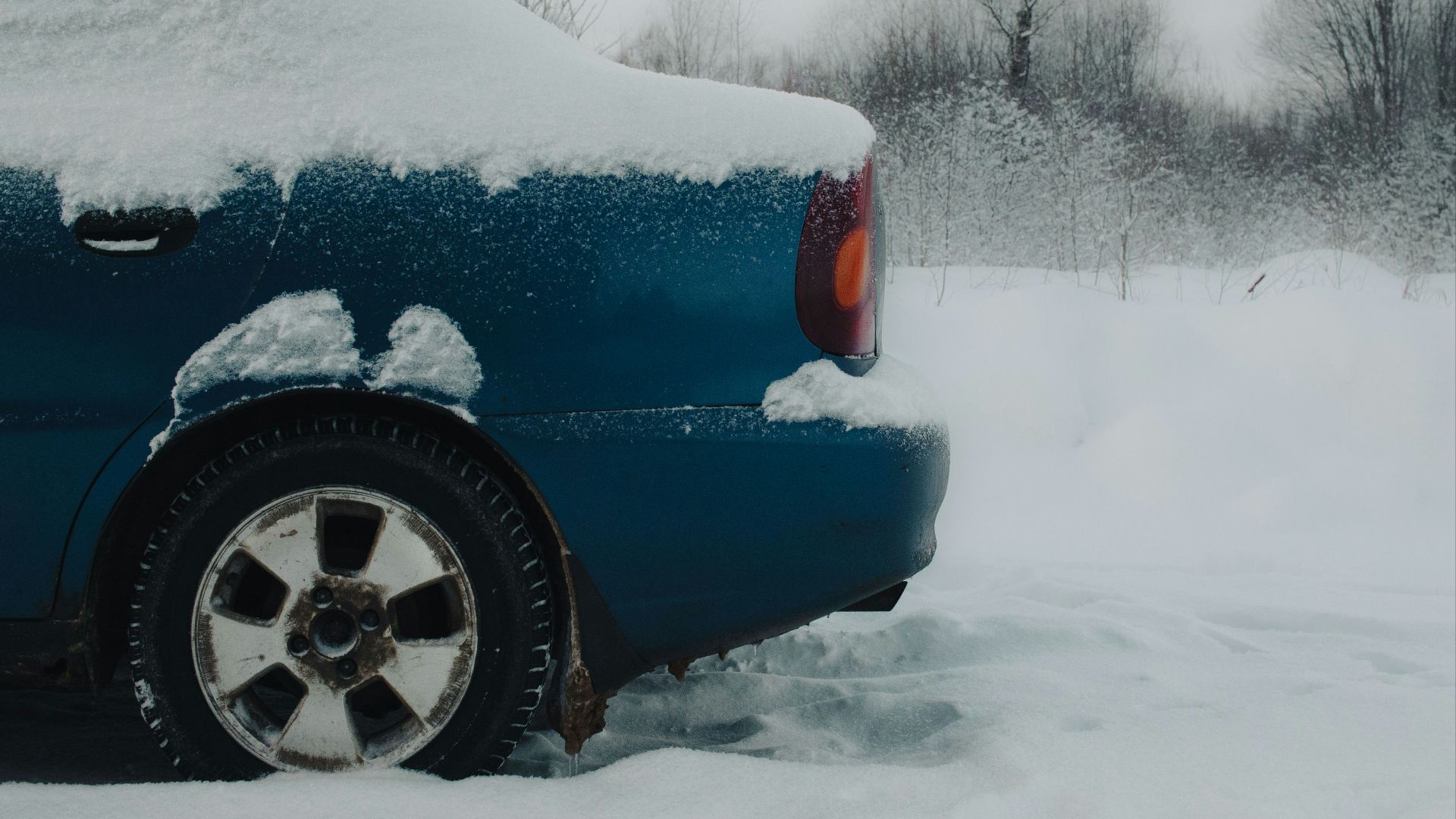 a blue car covered in snow on a snowy day