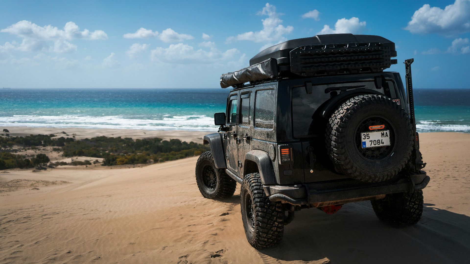 A jeep overlooks the ocean from a sandy dune.