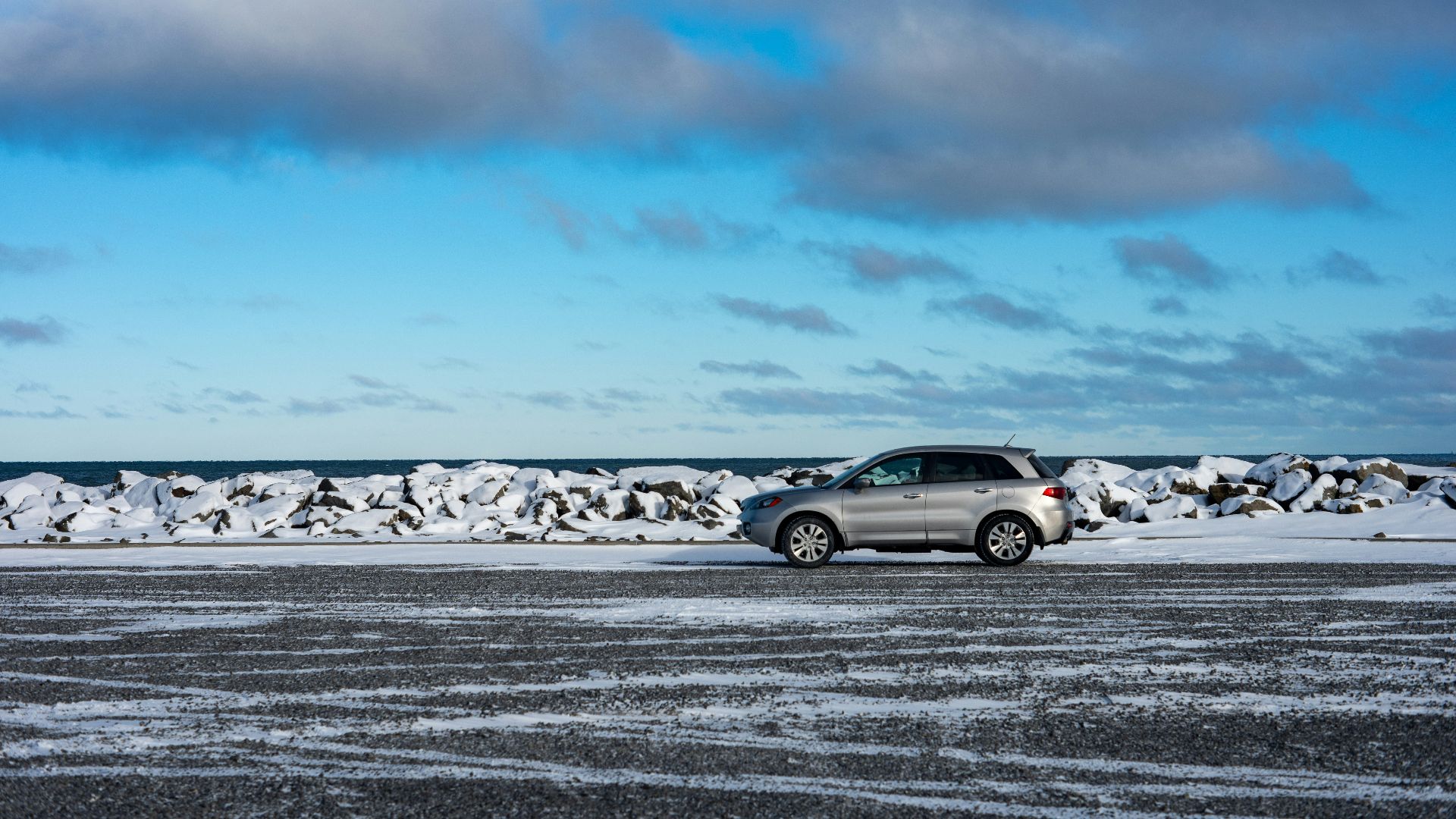Silver suv parked on a snowy landscape near the ocean.