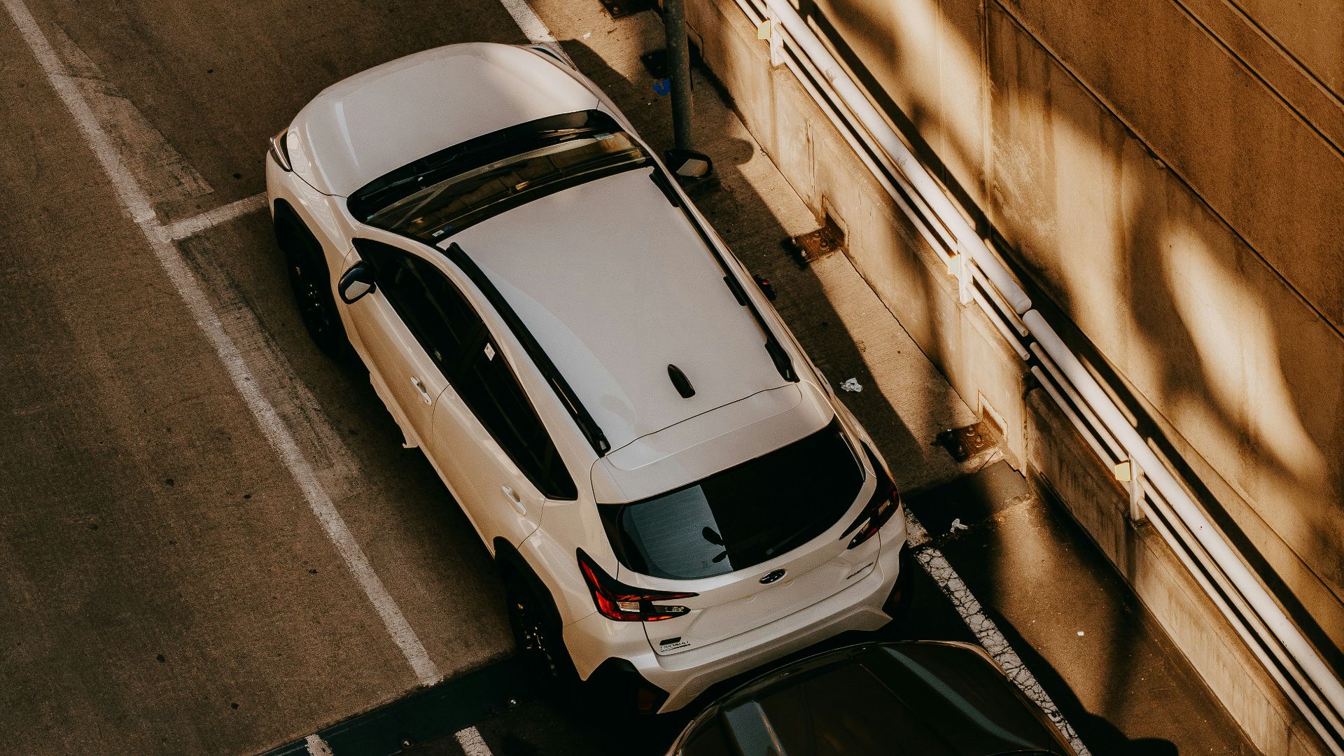 Two cars parked in a lot near a wall.