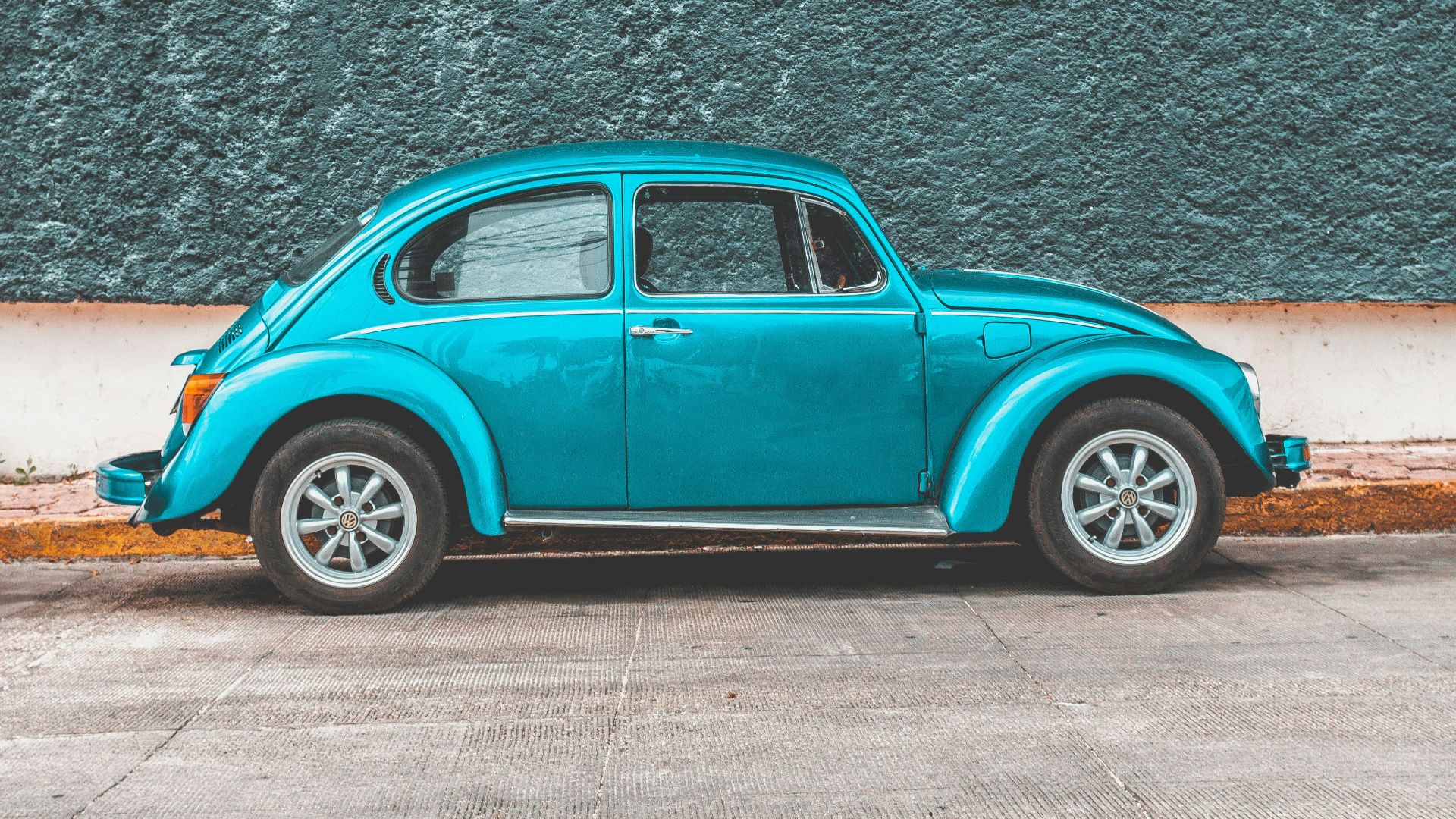 teal Volkswagen Beetle car parked beside sidewalk
