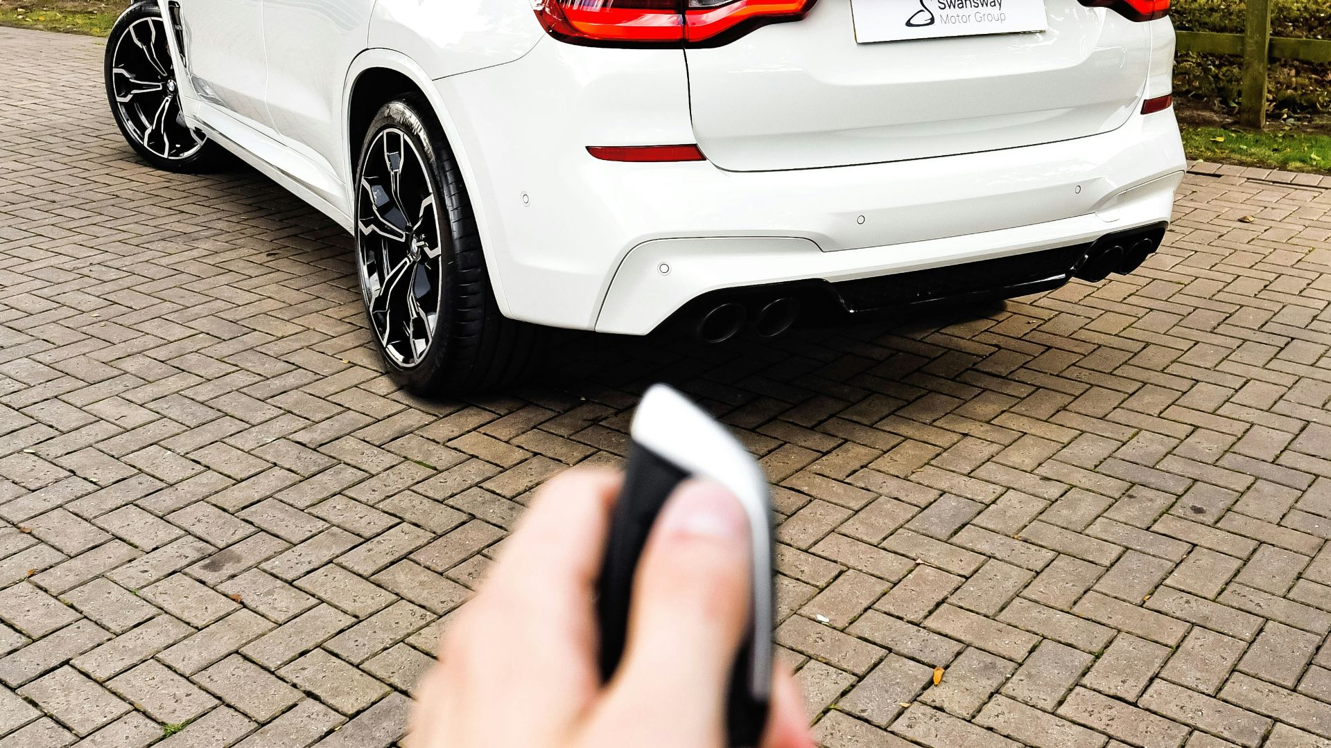 a hand holding a phone in front of a white car