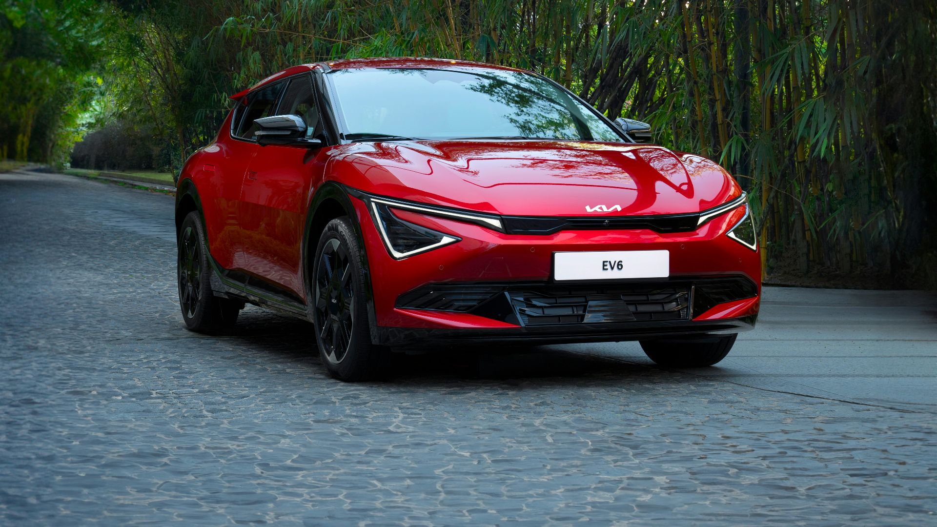 A red car driving down a street next to trees