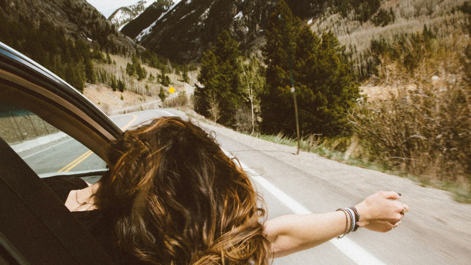 woman riding on vehicle putting her head and right arm outside the window while travelling the road
