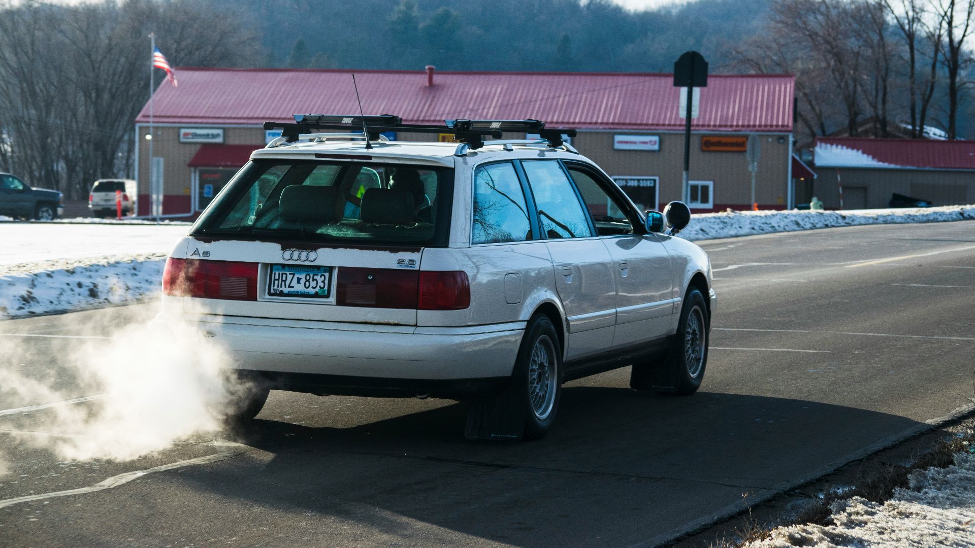 A white station wagon spews smoke while driving.