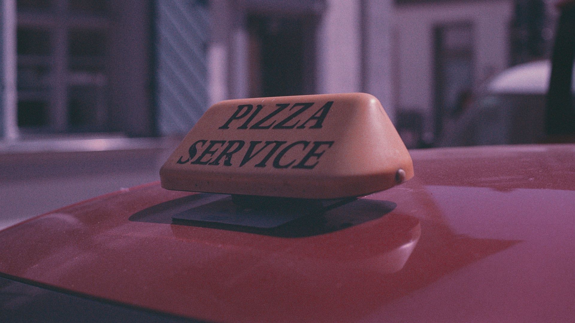 a pizza service sign on top of a red car