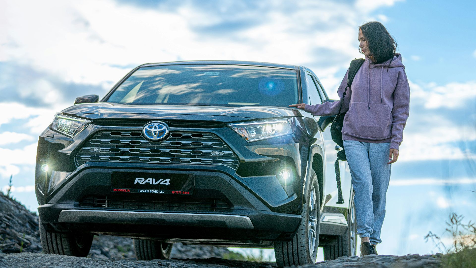A woman standing next to a car on a dirt road