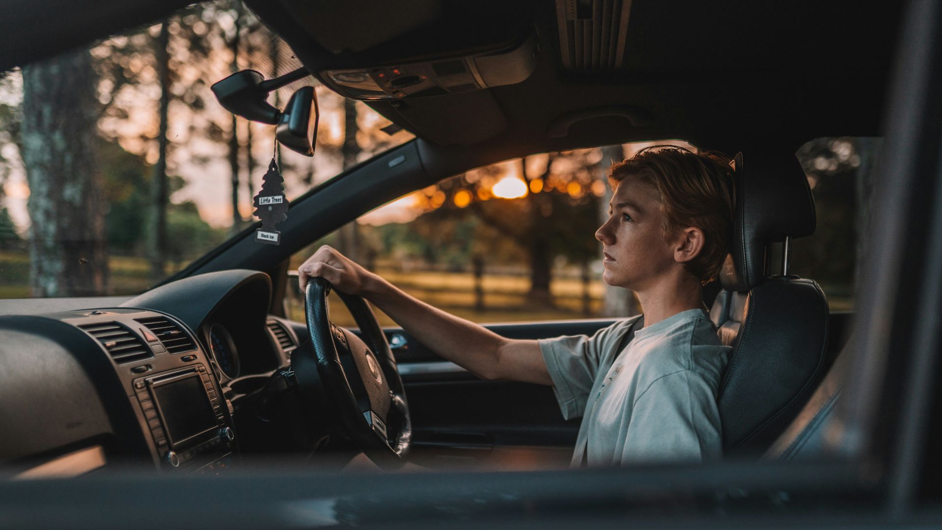 a man sitting in a car with his hand on the steering wheel