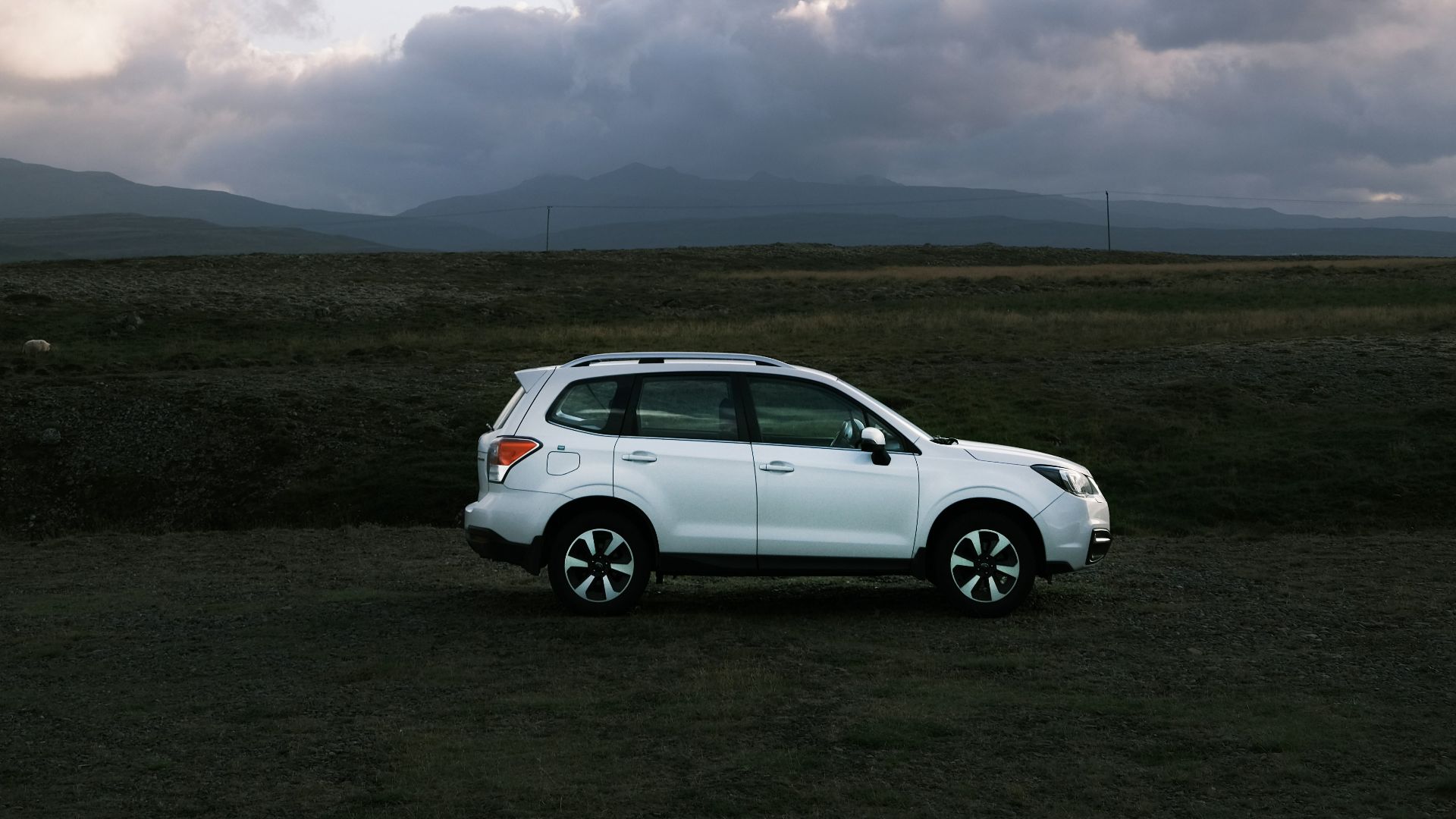 a white car parked in a field under a cloudy sky