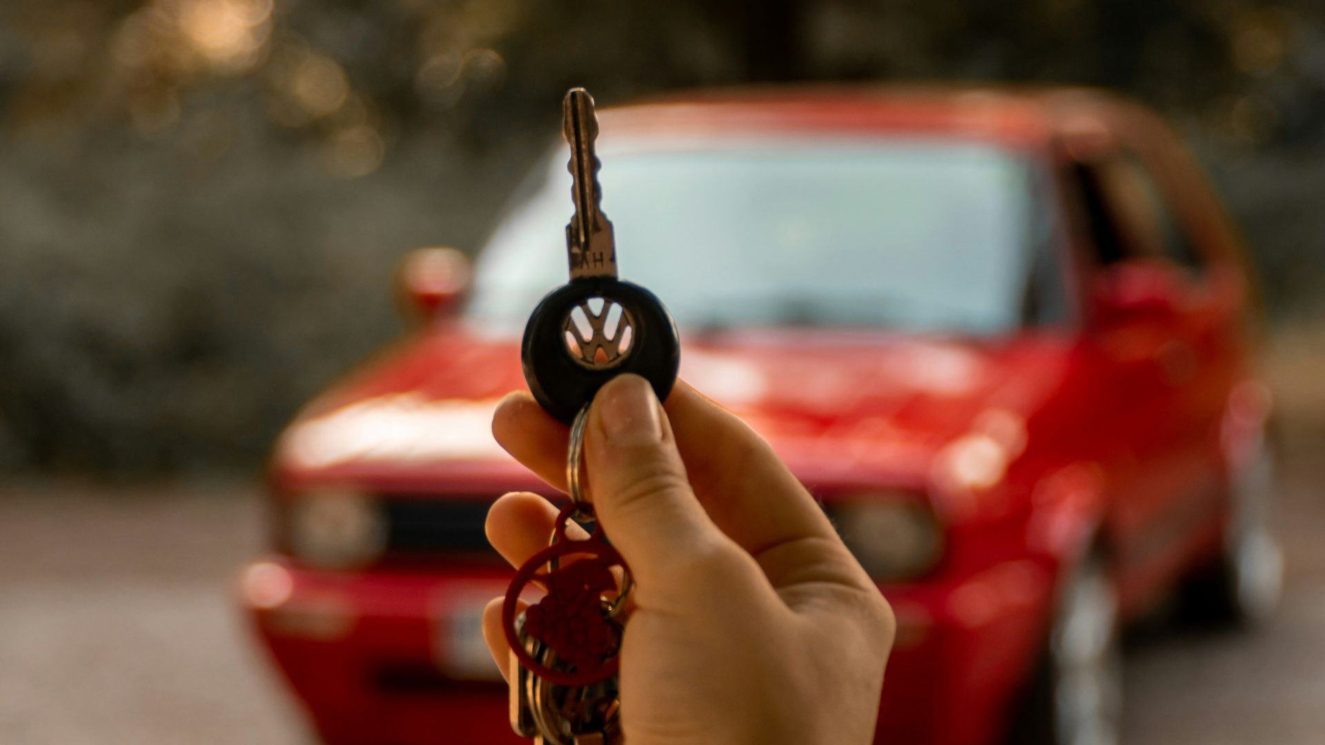 a person holding a car key in front of a red car
