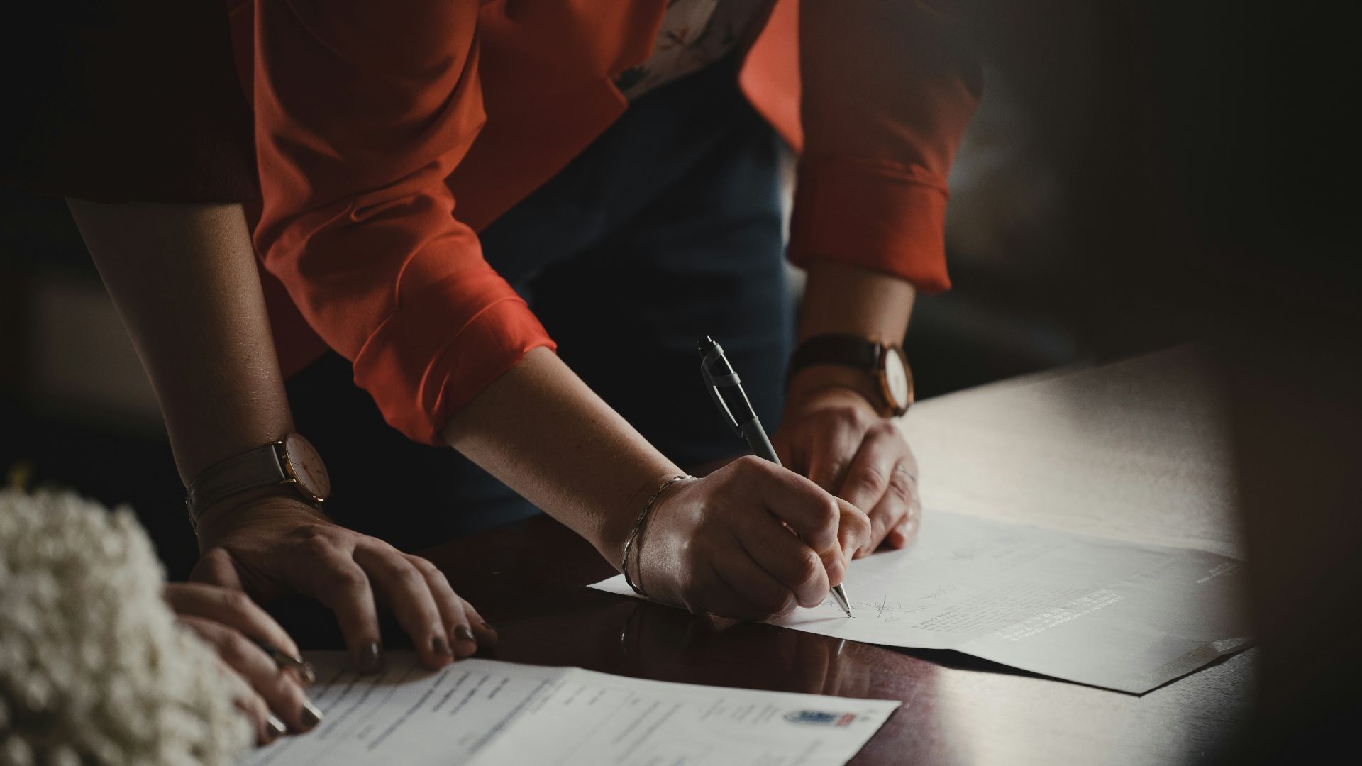 person in orange long sleeve shirt writing on white paper