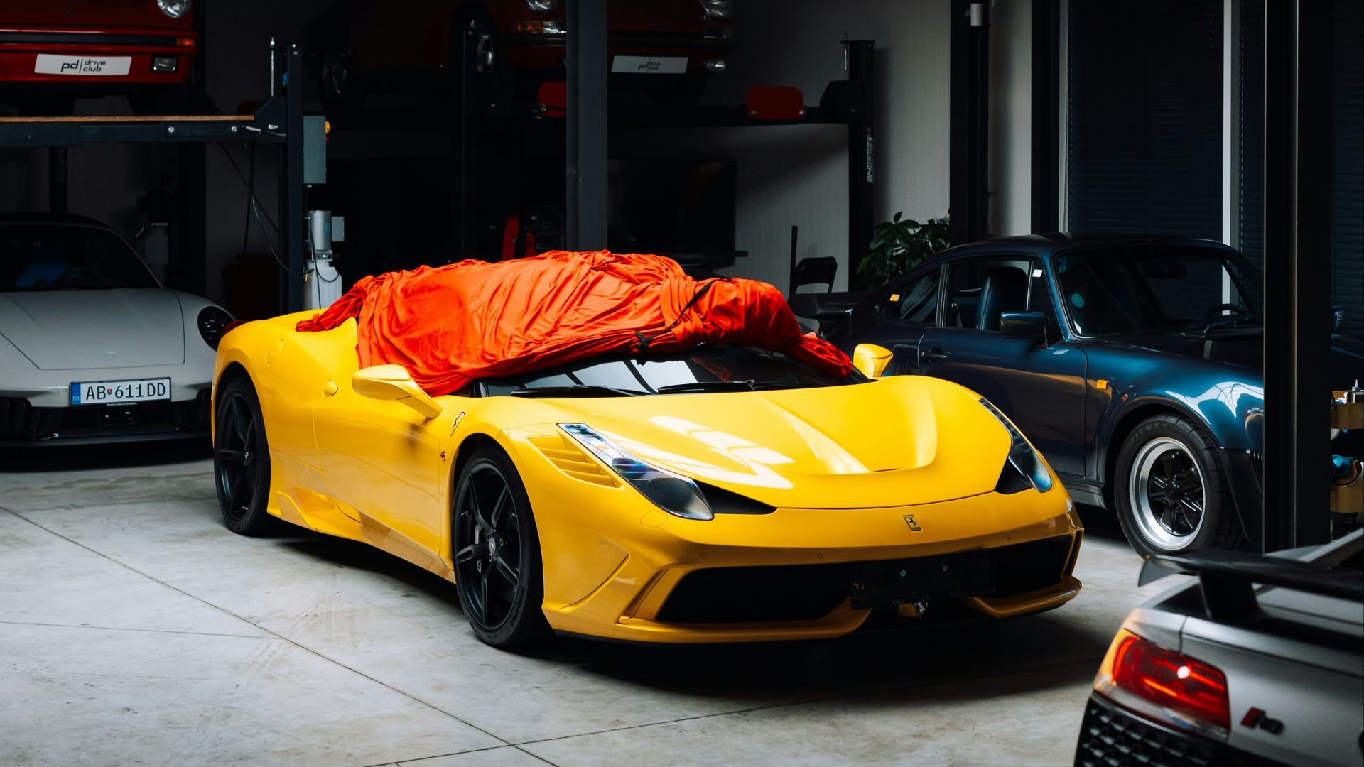 Yellow sports car covered with orange tarp in garage.