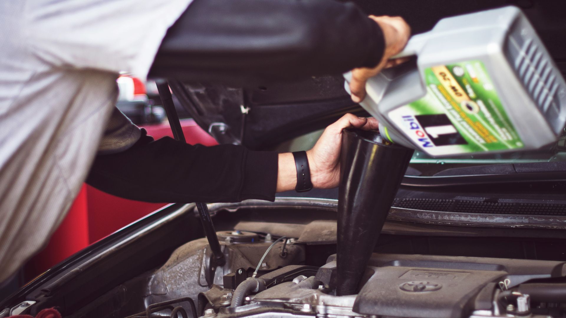 man refilling motor oil on car engine bay