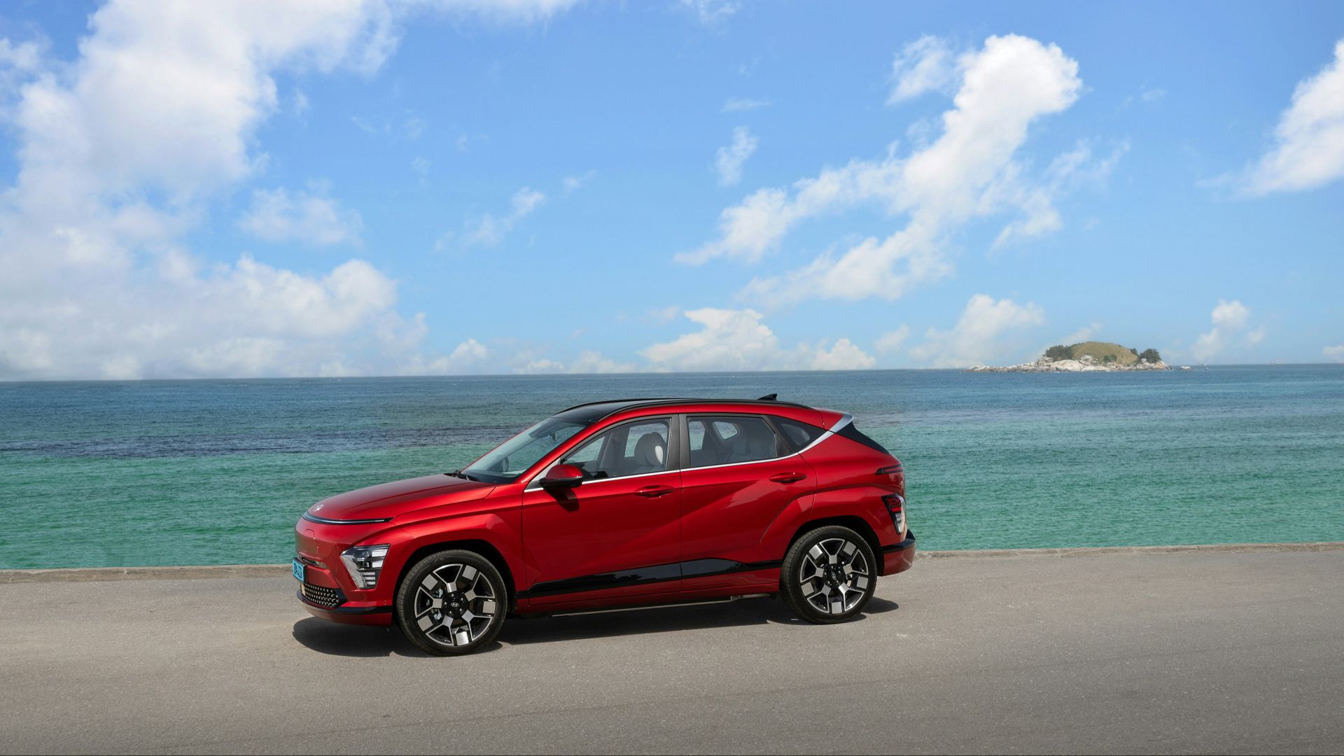 a red car parked on the side of a road next to the ocean