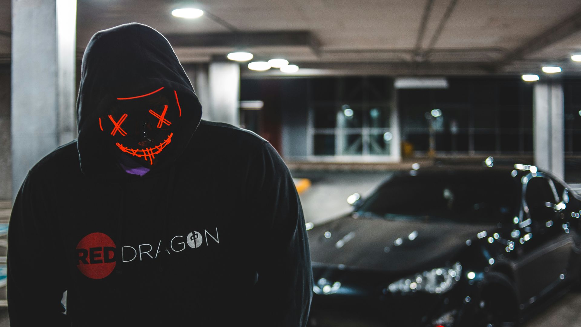 man in black hoodie standing beside black car
