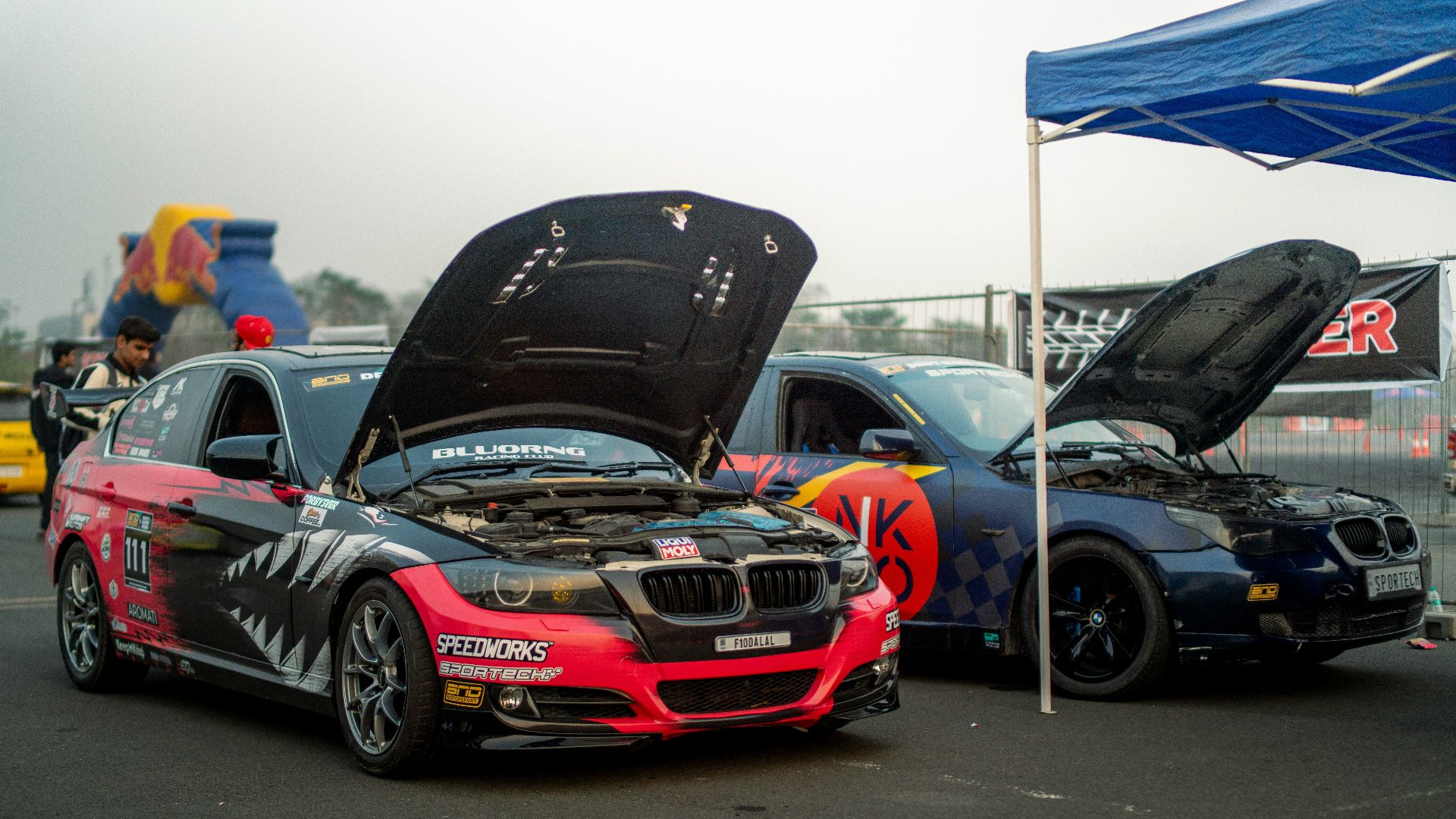 Two race cars with hoods open at an event