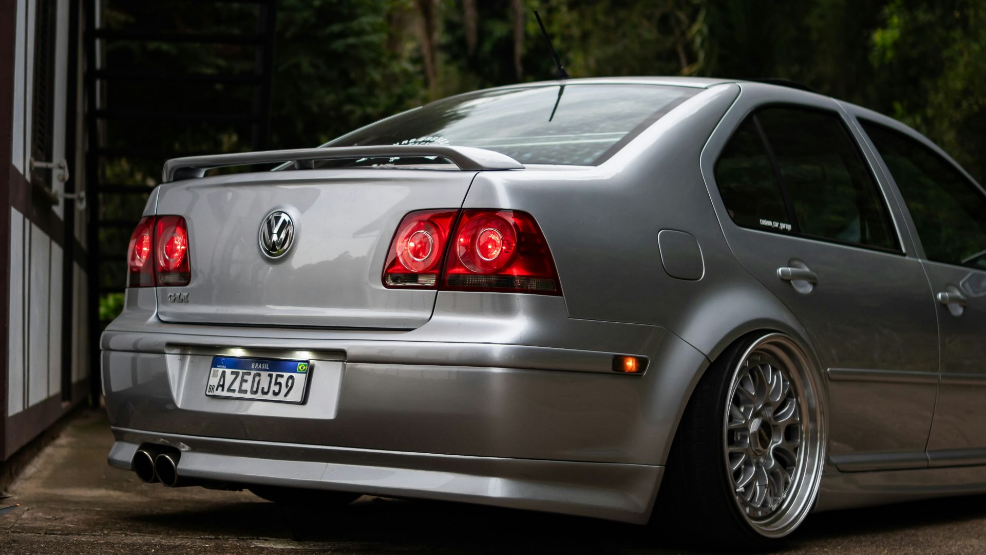 Silver sedan parked on a paved surface near trees.