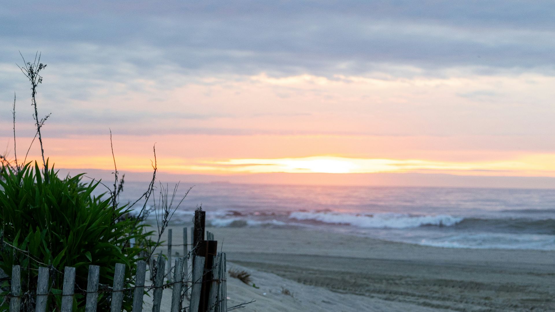 a fence on a beach with a sunset in the background